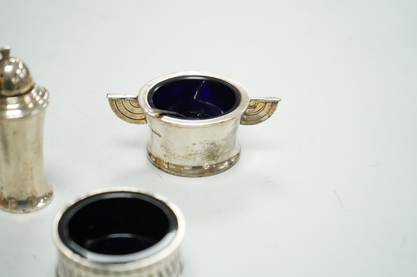 A George V Art Deco three piece silver condiment set and two spoons by William Adams Ltd, Birmingham, 1935, together with a pair of late Victorian pierced silver salts with blue glass liners and an Edwardian silver musta